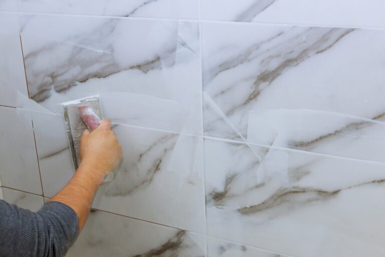 Grouting tiles male hand with the rubber applies grout on a seam between tiles